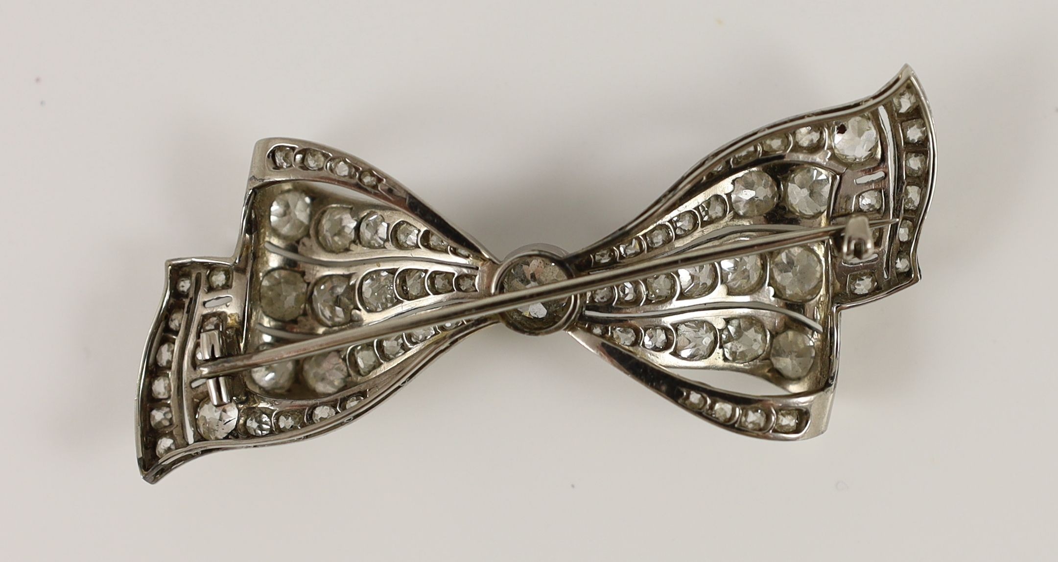 An early to mid 20th century white gold and graduated diamond cluster millegrain set ribbon bow brooch